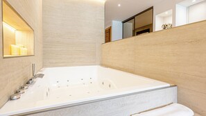 A modern bathroom with a large bathtub, a mirror, and a shelf with candles.