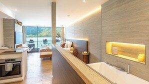 A modern bathroom with a large bathtub, a sink, and a mirror. There is a window with a view of a lake and hills. - Le Rivage Alpin - vue lac et spa (Tresserve)