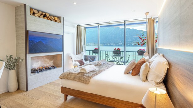 A bedroom with a large bed, a fireplace, a TV, and a balcony with a view of the mountains and lake. - Le Rivage Alpin - vue lac et spa (Tresserve)