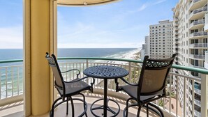 A balcony with a round table and two chairs, overlooking a beach and high-rise buildings. - Beach Colony West 13C (Pensacola)