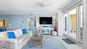 A living room with a white sofa, blue cushions, a wooden coffee table, a flat-screen TV, and a ceiling fan. - Beach Colony West 13C (Pensacola)