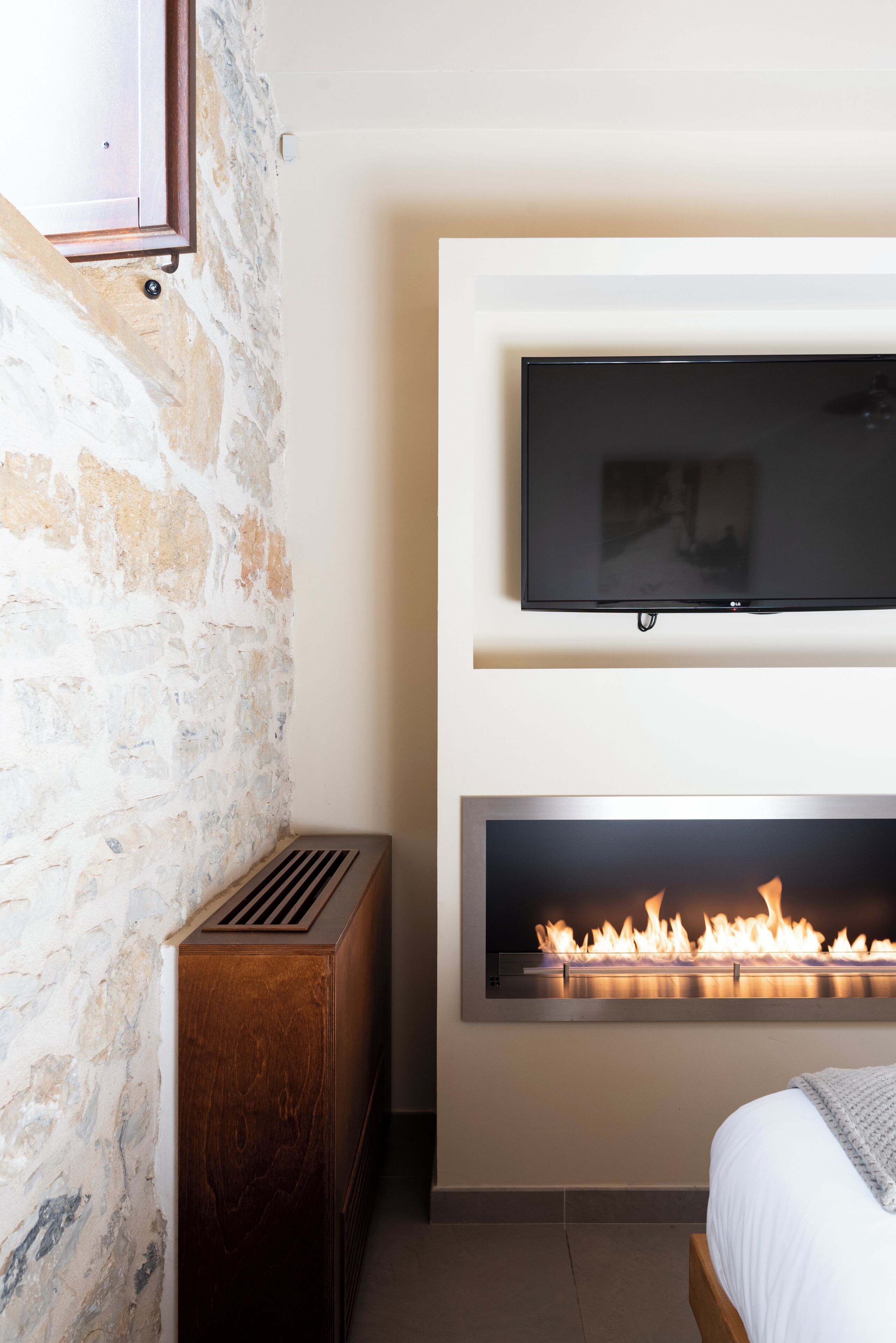 Un dormitorio con pared de piedra, televisor montado, chimenea y cama.