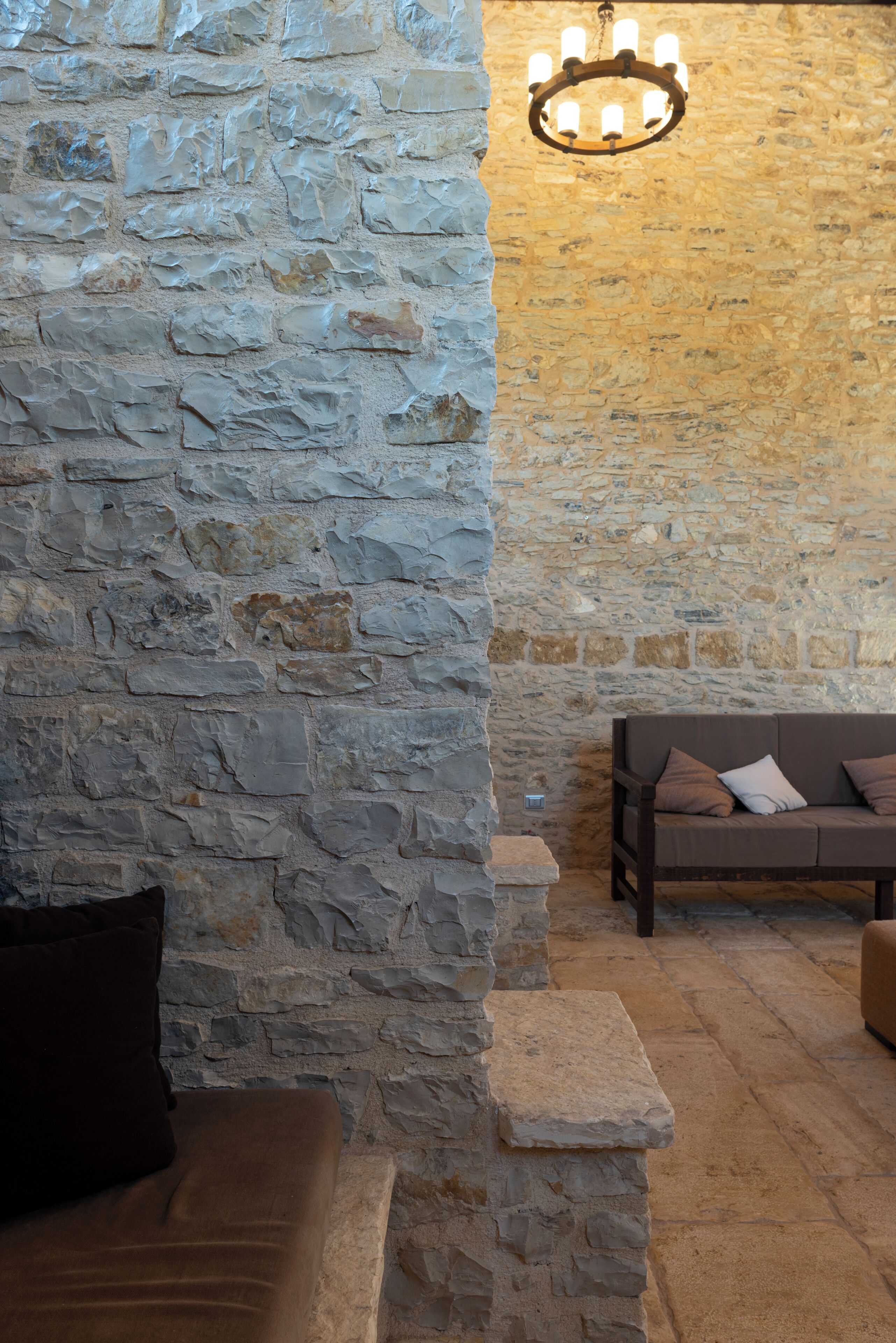 A stone-walled room with a wooden bench and a hanging light fixture.