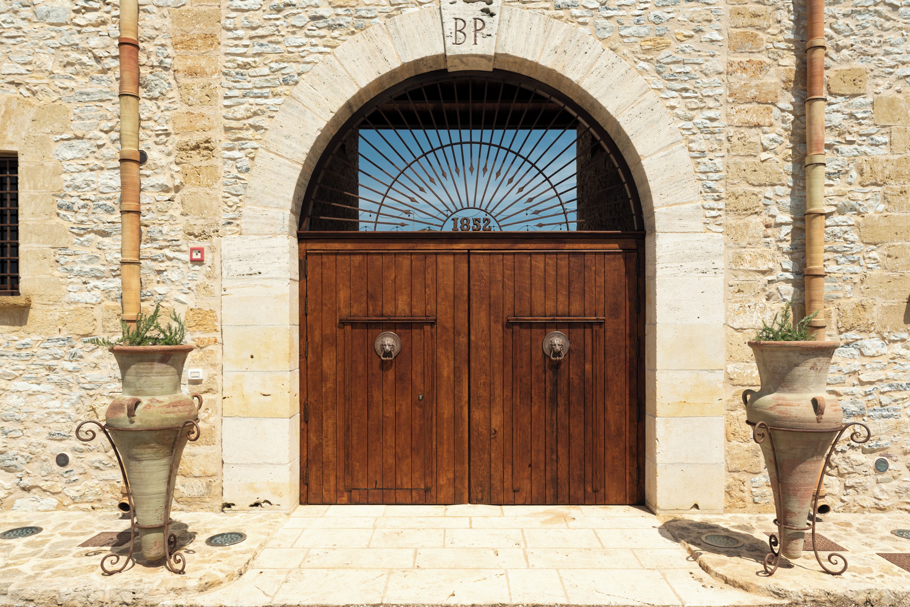 A stone building with a wooden double door, a date plaque, and two potted plants on either side.
