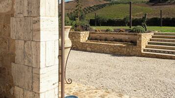 A stone archway leading to a gravel area with steps and a view of a vineyard and hills in the background.