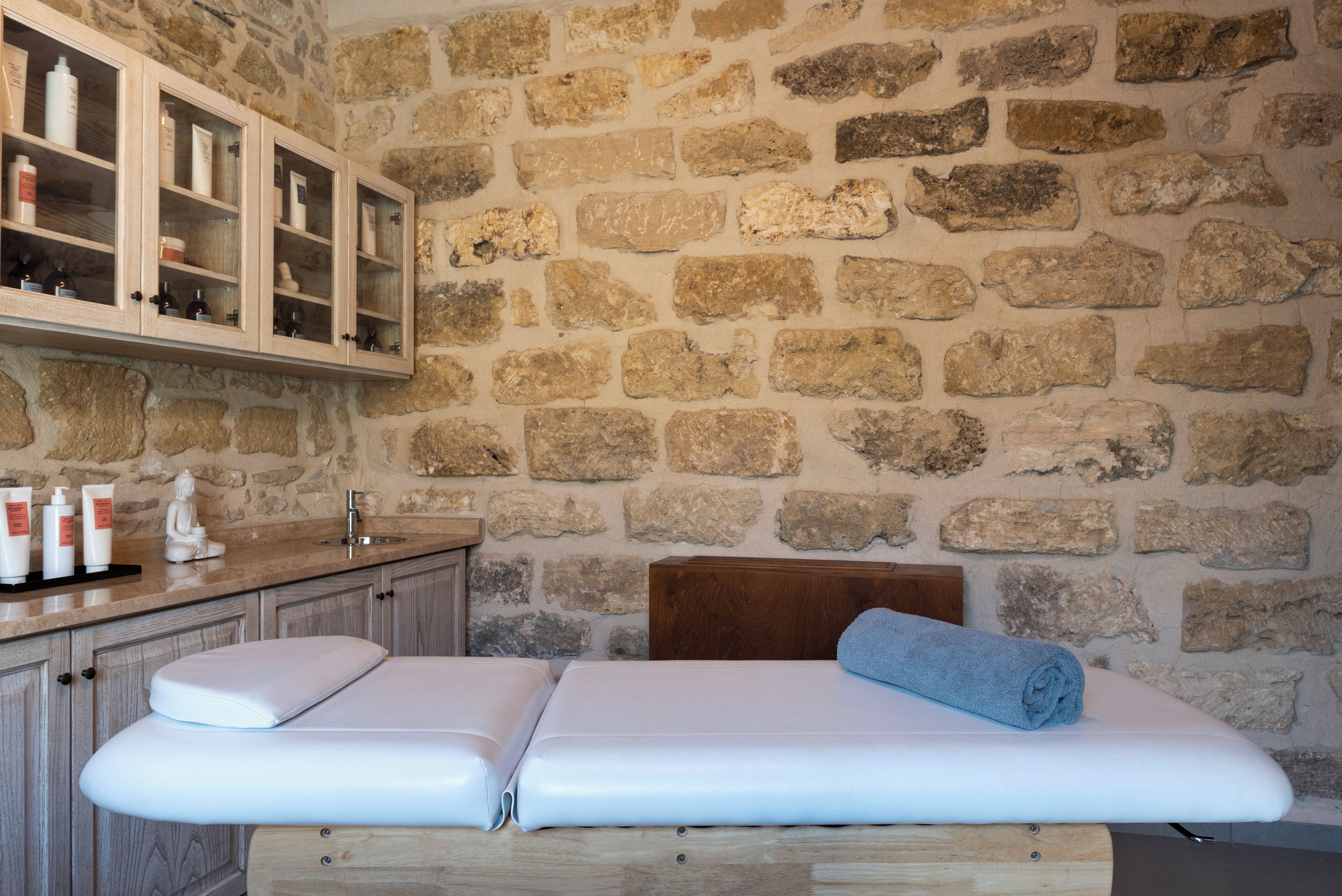 Une pièce aux murs de pierre, équipée d’une table de massage, de meubles en bois et d’un lavabo.