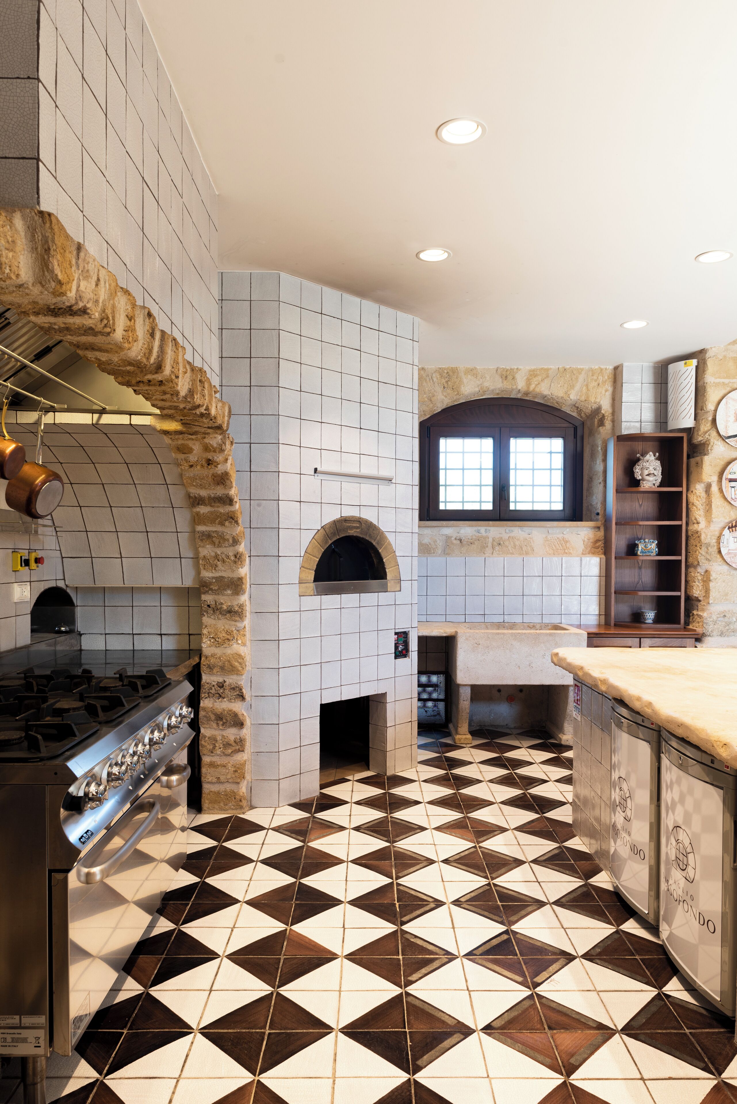 Una cocina con un arco de piedra, paredes con azulejos, un horno central y un suelo estampado.