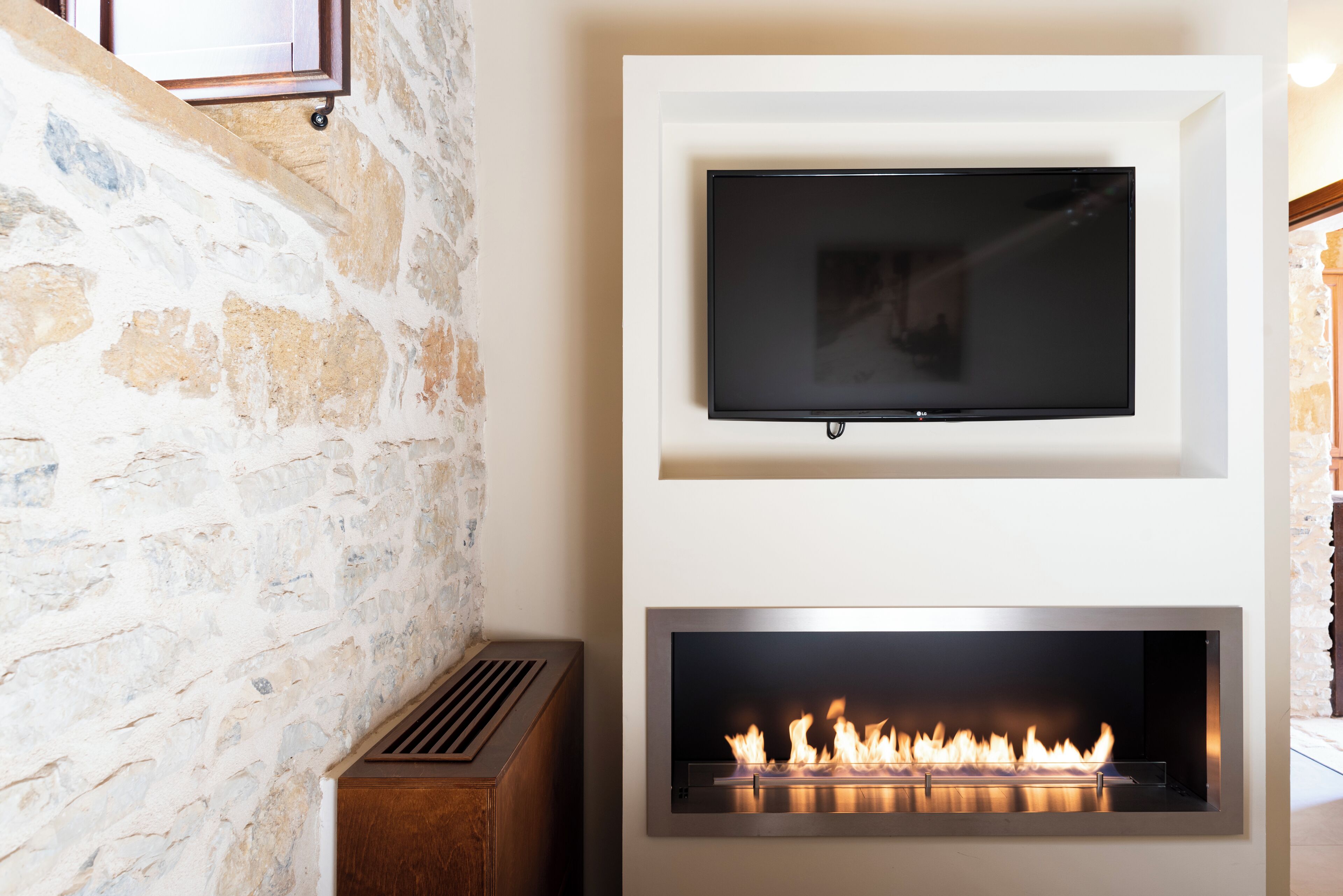 A stone wall, a mounted TV, and a fireplace with visible flames.