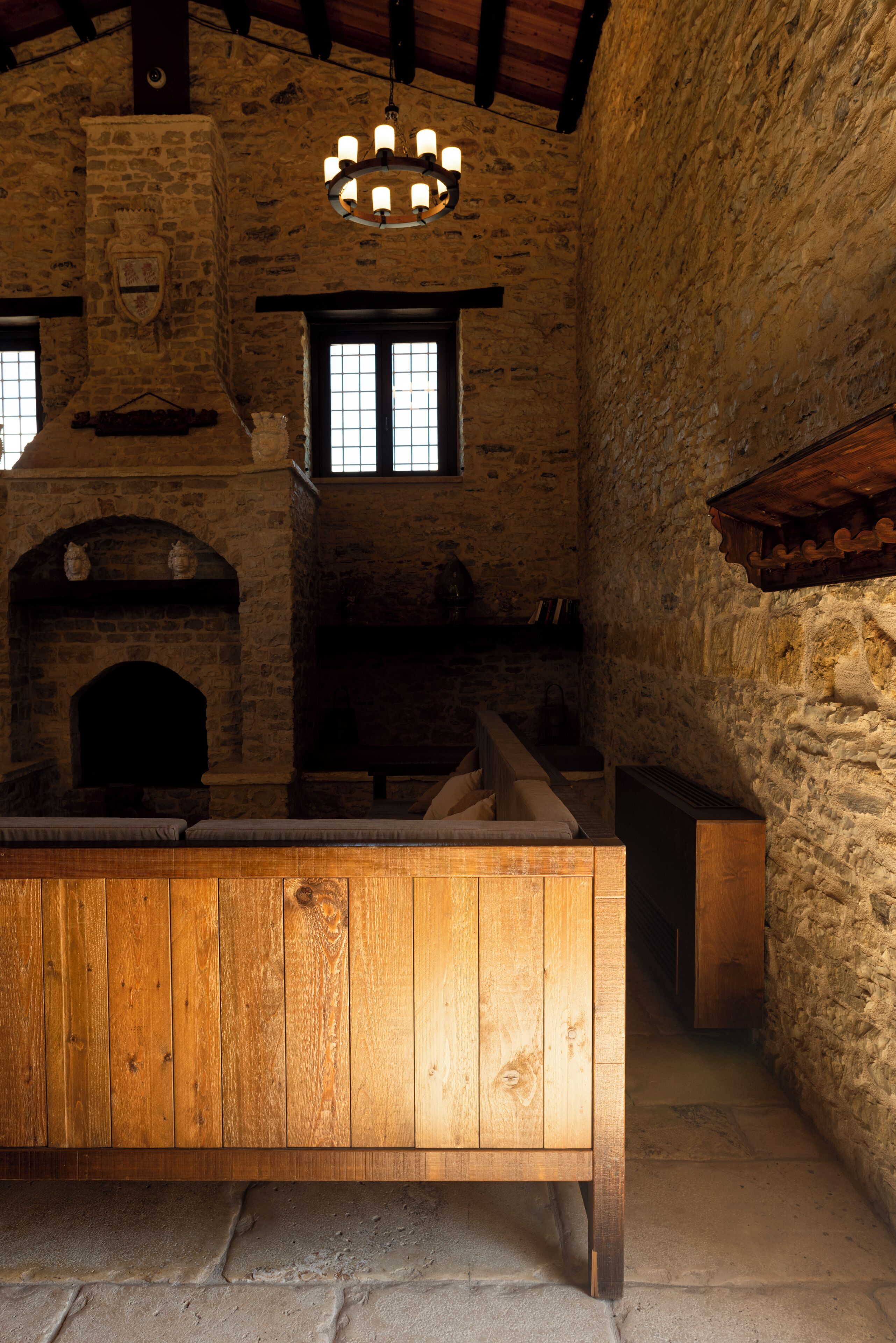 A rustic stone interior with a wooden bench, stone fireplace, and a chandelier.