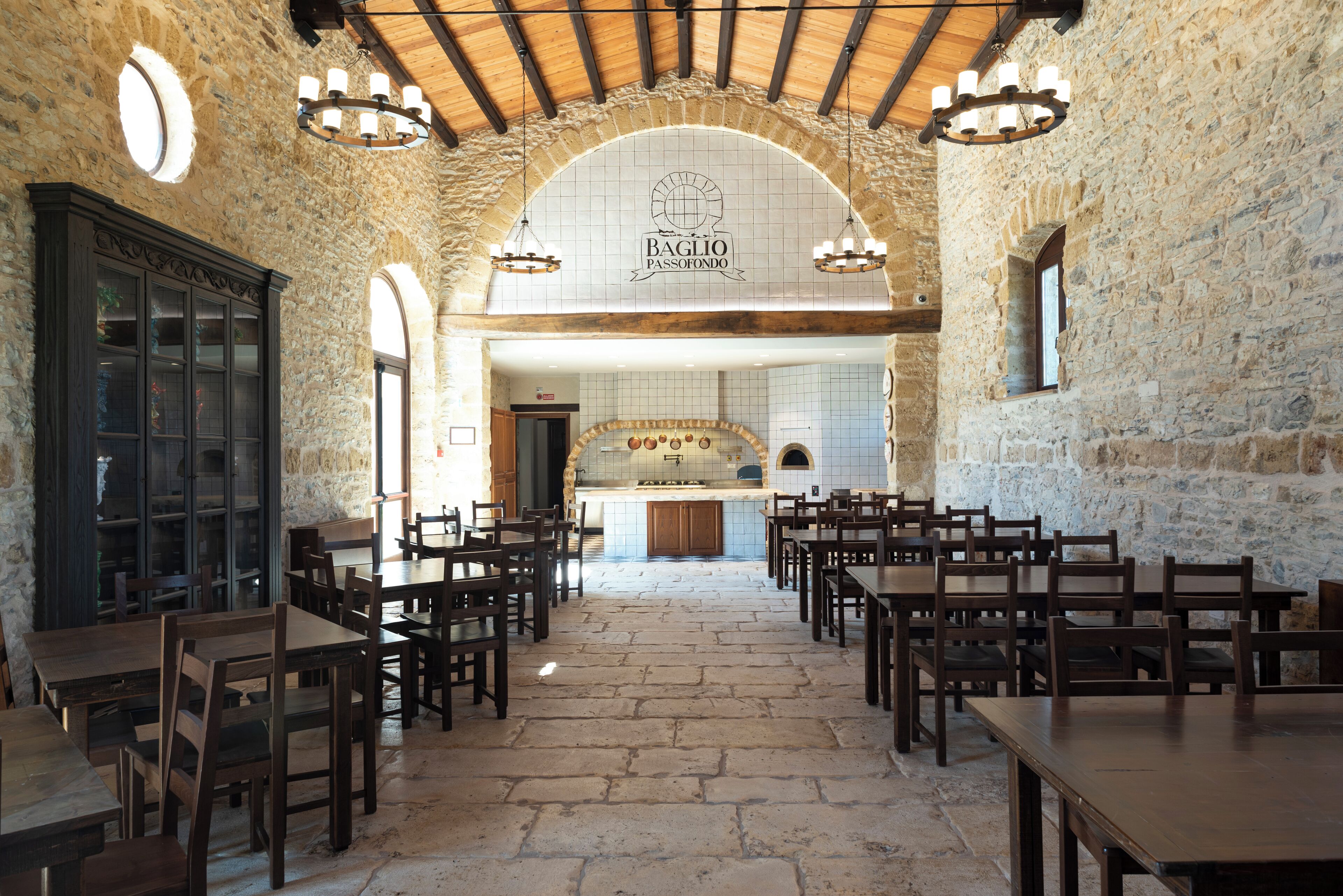 Un restaurante con paredes de piedra, mesas y sillas de madera, una zona de cocina y un letrero que dice "BAGLIO PASSO FONDO".