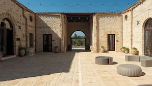 An outdoor courtyard with stone walls, arched doorways, and potted plants. - Tenute Baglio Passofondo (Alcamo)