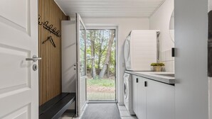 Une cuisine moderne équipée d’un lave-linge et d’un sèche-linge intégrés, d’un banc et offrant une vue sur les arbres à l’extérieur.