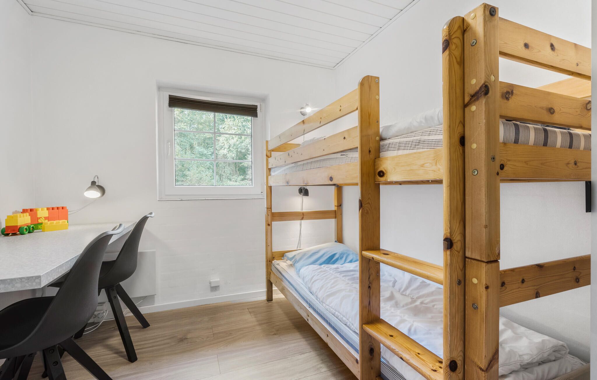 Een slaapkamer met stapelbed, bureau en stoelen, een raam en een lamp.