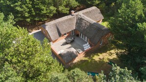 Une maison au toit de chaume, entourée d’arbres denses.