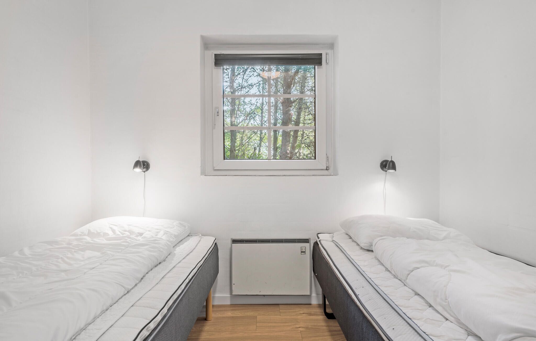 Une petite pièce lumineuse, avec deux lits simples, une fenêtre donnant sur les arbres et un radiateur fixé au mur.
