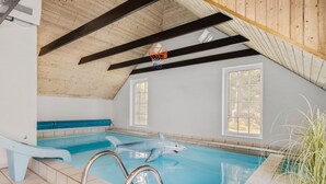 Une piscine intérieure avec un flotteur en forme de requin, des poutres en bois et de grandes fenêtres.