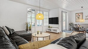 Un salon moderne avec un canapé en cuir noir, une table basse ronde et un téléviseur fixé au mur.
