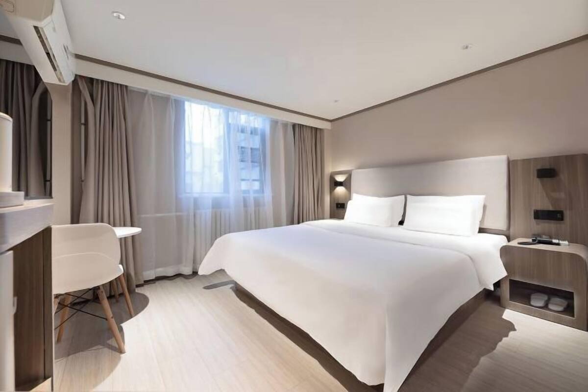 A modern hotel room with a large bed, a desk, and a chair.