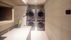 A modern laundry room with two stacked washing machines, a small potted plant, and a wooden bench. - HanTing Hotel (Zhengzhou Zijingshan Subway Station) (Zhengzhou)