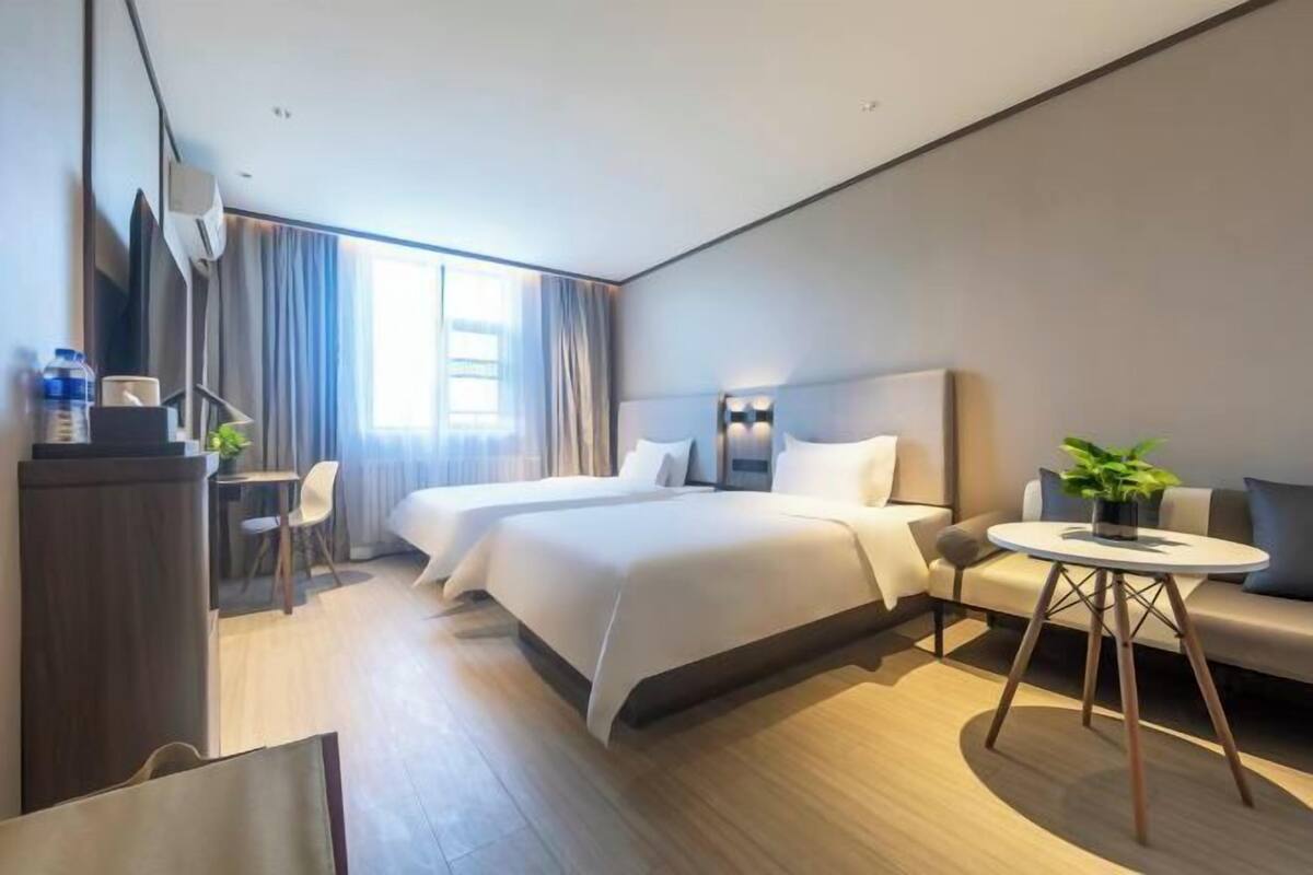 A modern hotel room with a large bed, a desk, a chair, a small table with a plant, and a sofa.
