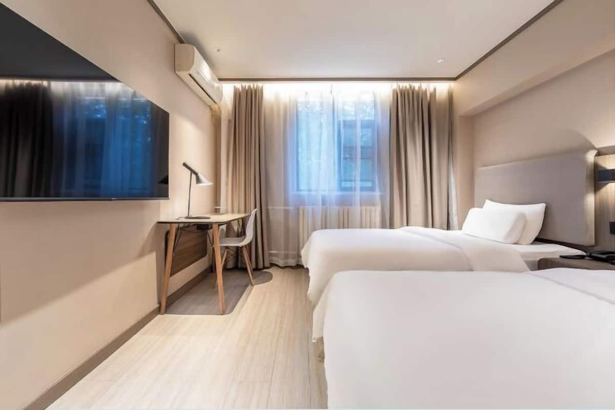A hotel room with two beds, a desk, a chair, a TV, and a window with curtains.