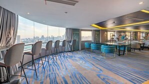 Egy modern szállodaszoba, melynek páratlan panorámája a városra nyílik, ívelt formájú ülősarokkal és kék színű díszítésekkel ellátott bár-/lounge-résszel.