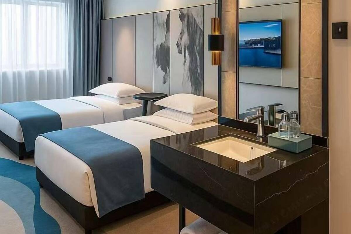 A hotel room with two beds, a large mirror, a TV, and a modern bathroom.