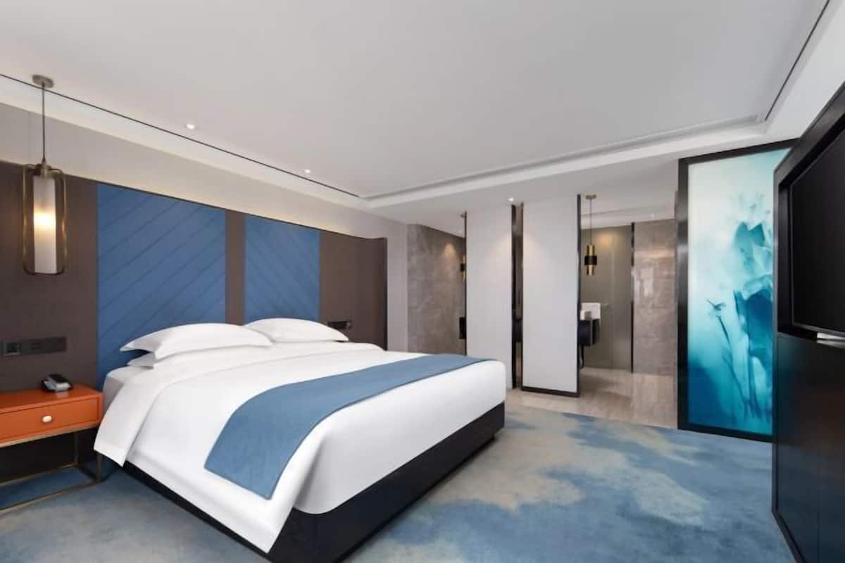 A modern hotel room with a large bed, a desk, and a bathroom visible through an open door.