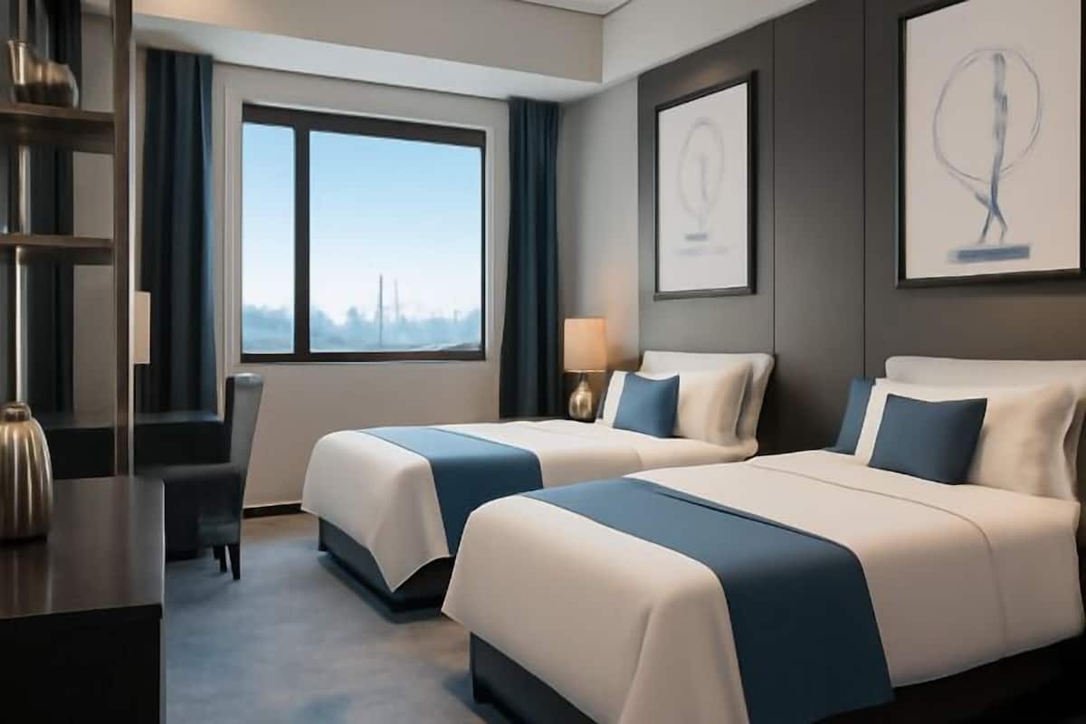 A hotel room with two beds, a desk, a chair, and a window with a view.