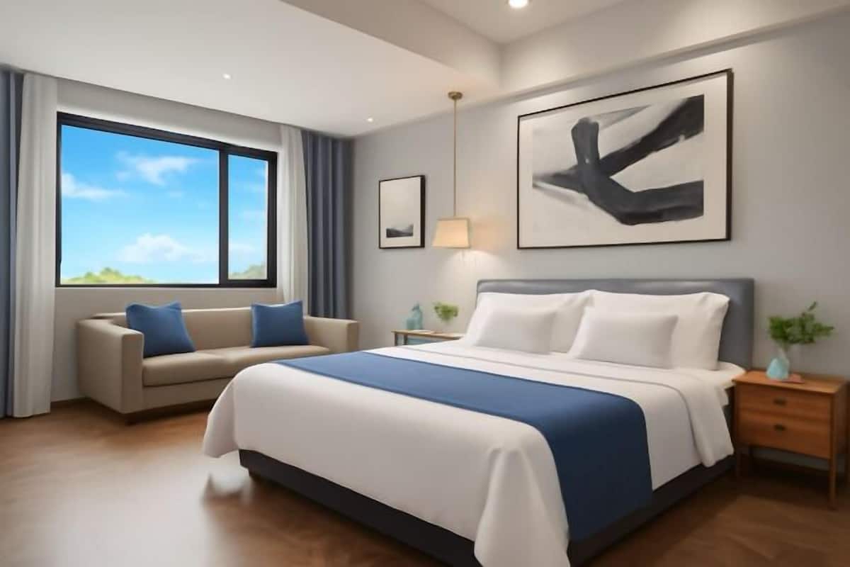 A modern hotel room with a large bed, a sofa, a bedside table, and a large window.