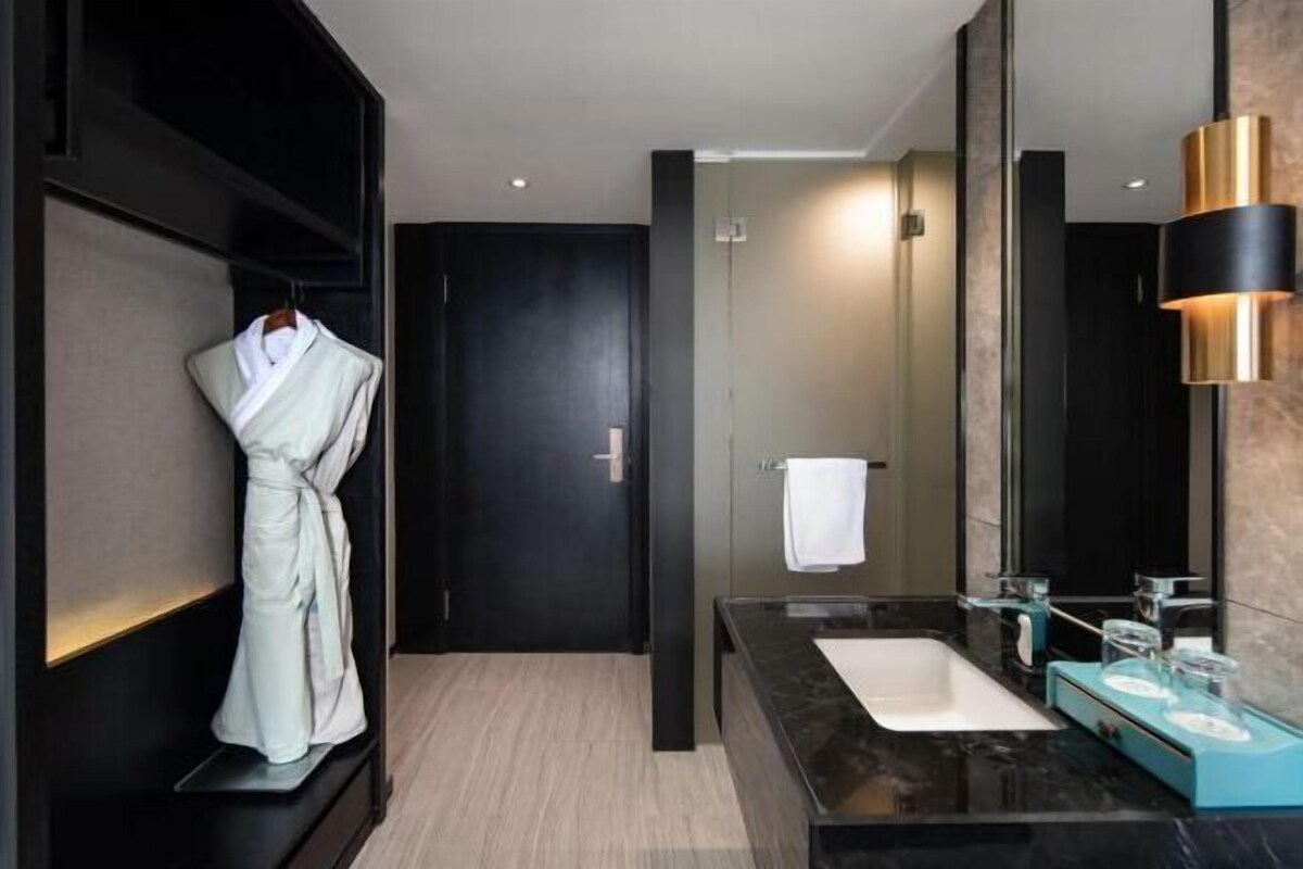 A modern bathroom with a black vanity, a large mirror, and a robe hanging on a rack.