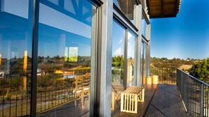 A balcony with a wooden bench, glass walls, and a view of a landscape with trees and buildings. - Acogedora cabaña en el bosque Tapalpa (Tapalpa)