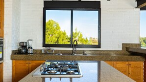 A kitchen with a gas stove, a coffee maker, and a window with a view of trees. - Acogedora cabaña en el bosque Tapalpa (Tapalpa)