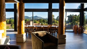 A spacious indoor area with large windows, wooden flooring, and a dining area with tables and chairs. - Acogedora cabaña en el bosque Tapalpa (Tapalpa)