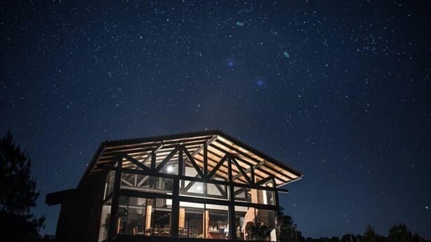 A two-story building with a wooden framework and large windows, under a starry night sky. - Acogedora cabaña en el bosque Tapalpa (Tapalpa)