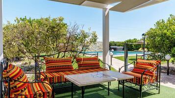 Relax in a comfortable outdoor seating area with a sofa set and small table, overlooking a swimming pool and lush greenery.
