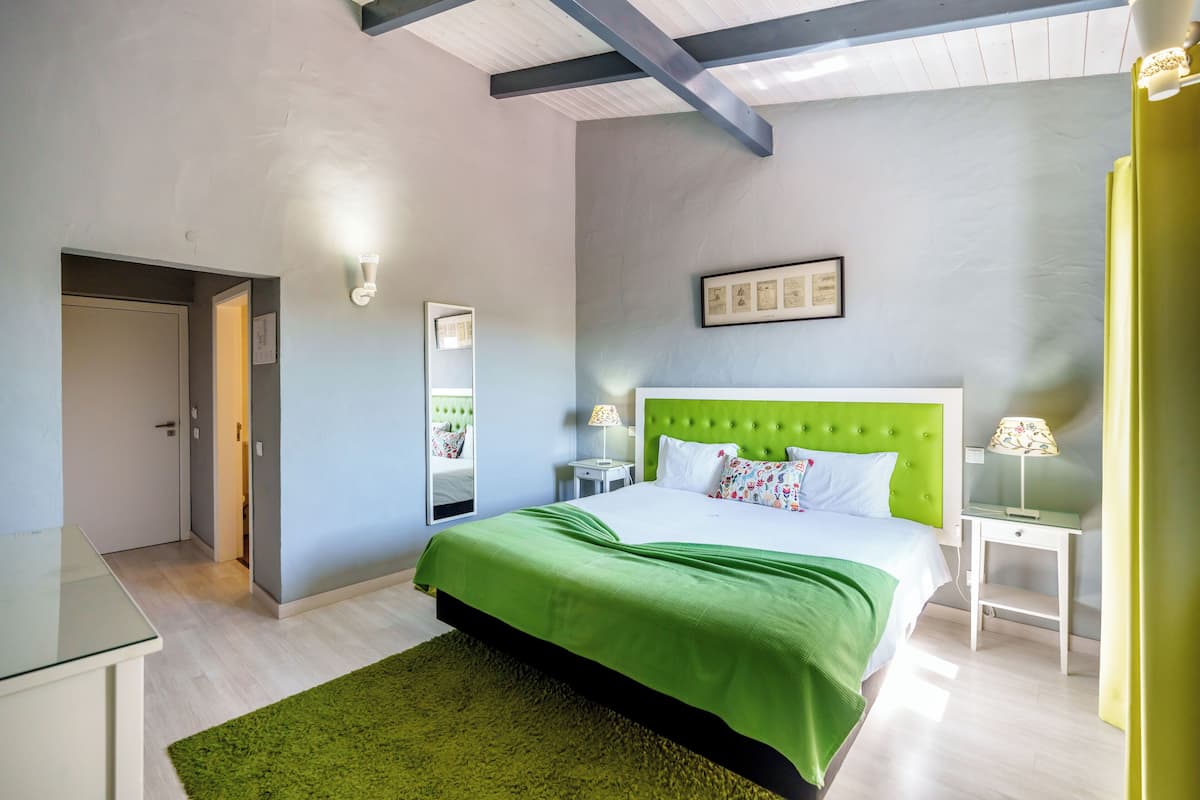 Une chambre avec une couvre-lit verte, une tête de lit verte, une table de chevet avec une lampe et un tableau encadré au mur.