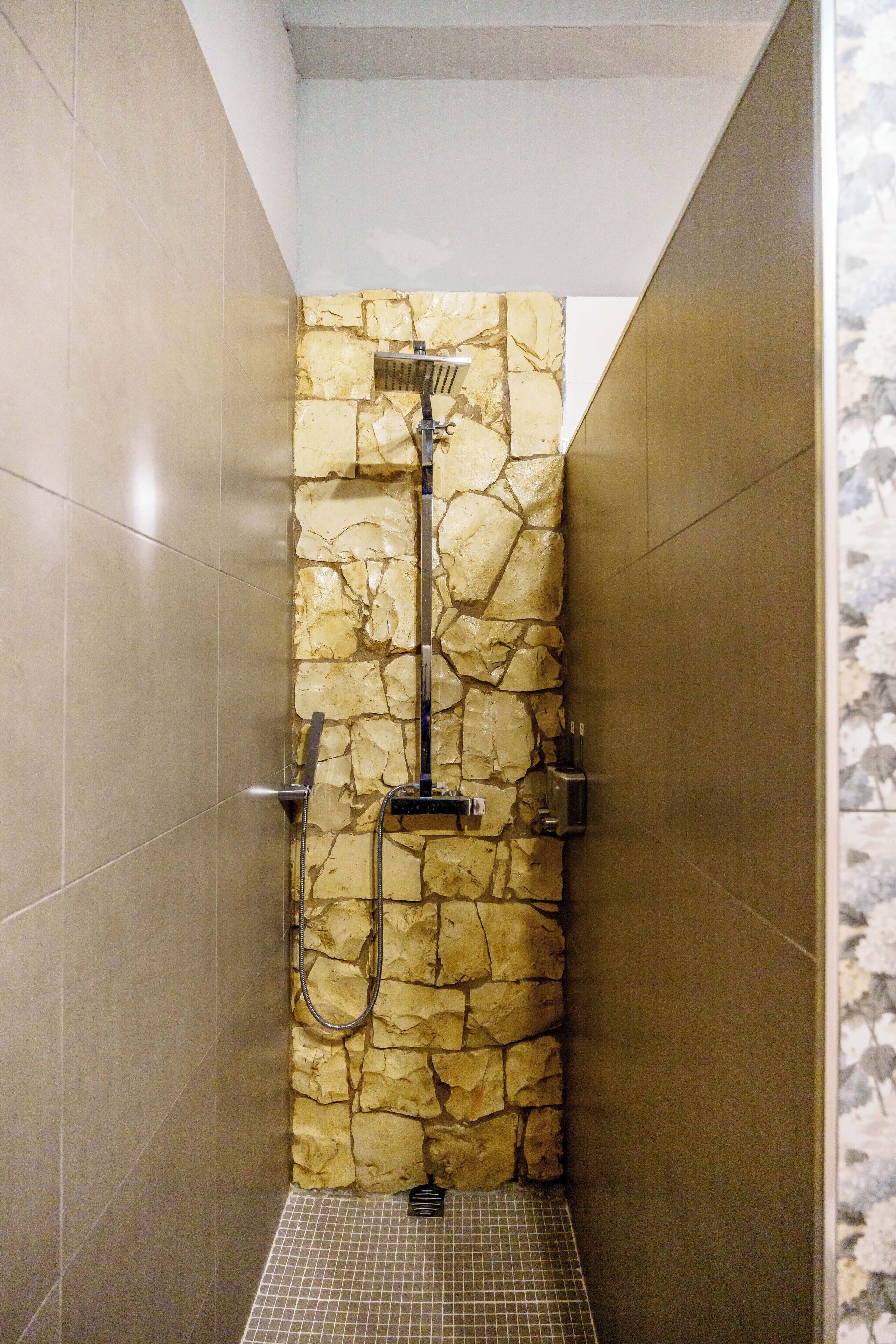 Ducha con pared de piedra, suelo de baldosas y cabezal de ducha.