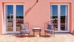 Une terrasse avec deux chaises et une petite table, une porte-fenêtre coulissante et un luminaire au-dessus.