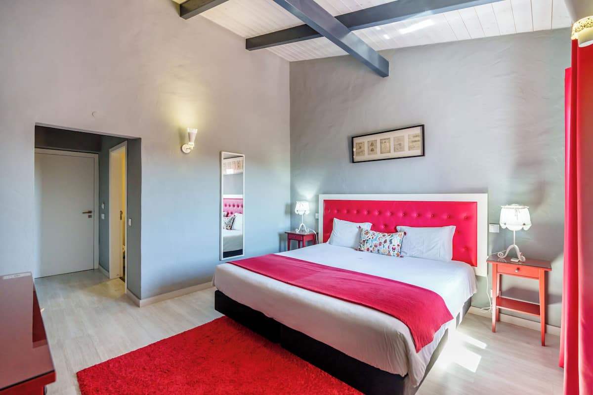 Une chambre moderne avec un grand lit, un mur d’accent rouge et un miroir.