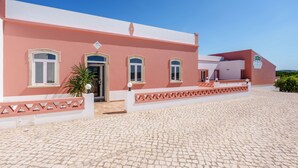 Un bâtiment rose avec une allée pavée, une clôture blanche et un petit jardin.