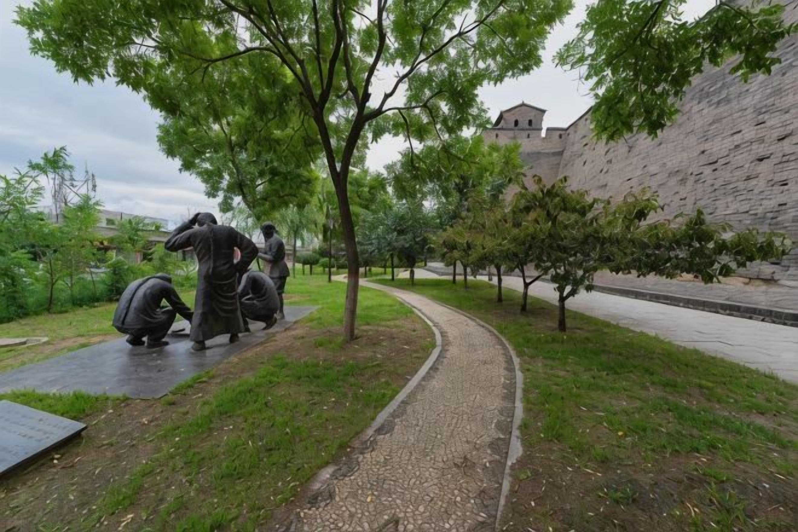 A pathway with sculptures, a brick wall, and a building in the background.