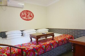 A hotel room with a bed, a small wooden table, a colorful bedspread, a red wall decoration, and a tiled wall. - Qininn Qiaozhai Minsu Fengqing Branch (Pingyao County)