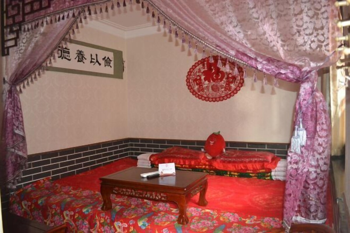 A room with a red carpet, a wooden table, a red sofa, and a decorative red hanging ornament.