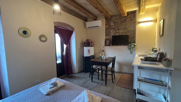 A cozy room with a bed, a desk, a chair, a small table, and a stone wall.