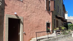 A building with a large door, a small window with flowers, and a stone staircase leading to a balcony.