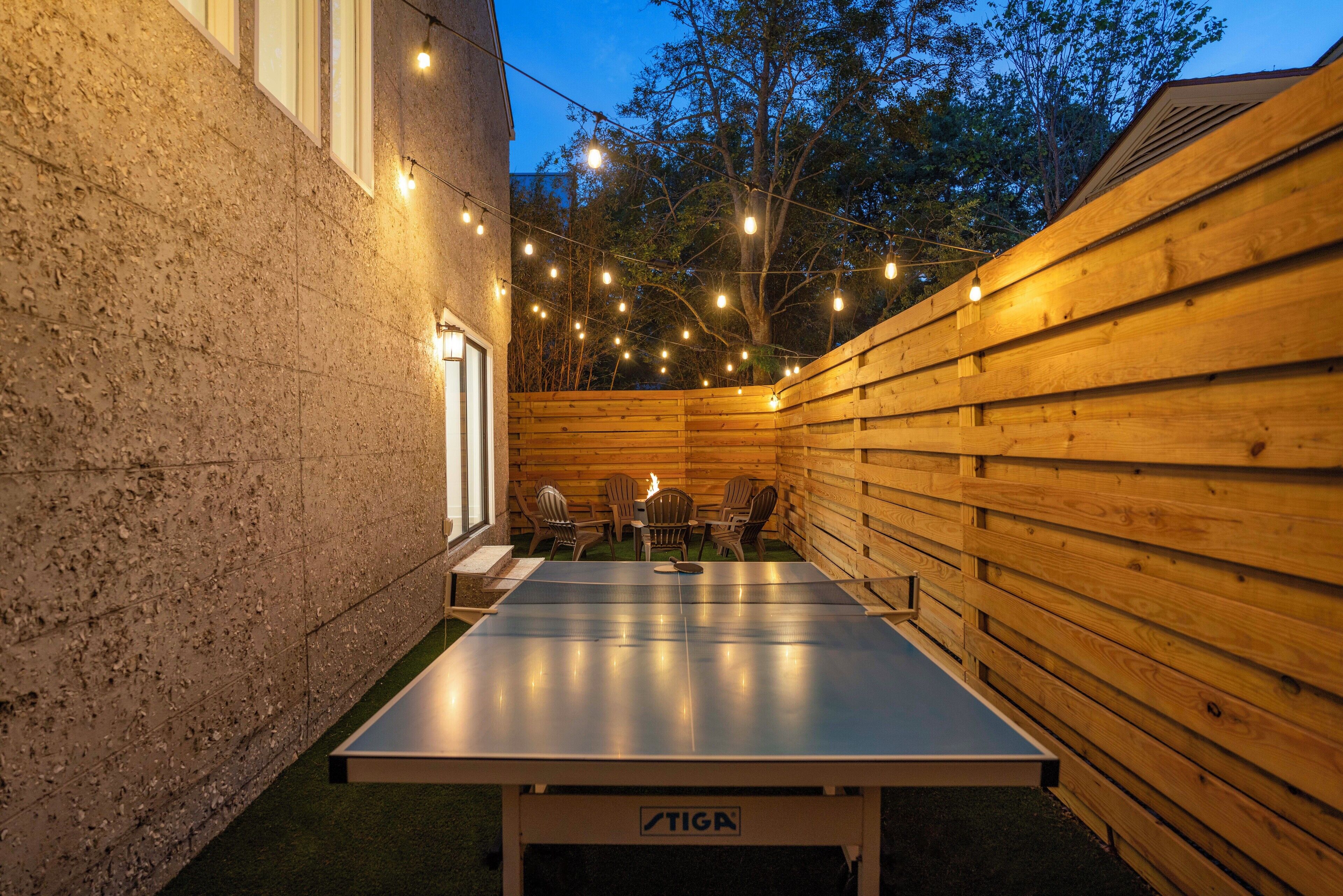 Una mesa de ping pong en un espacio al aire libre con paredes de madera y luces colgantes.