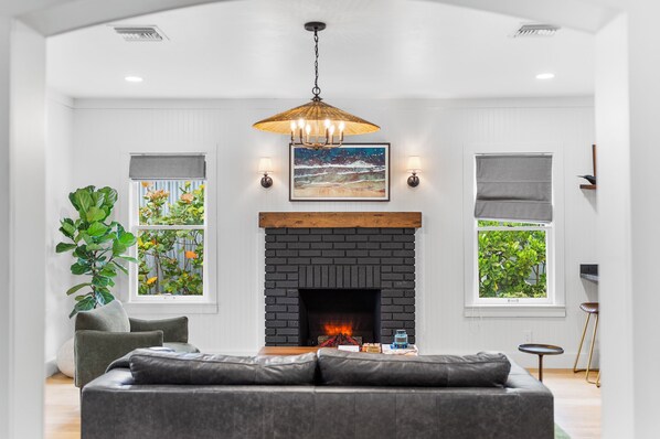 A modern living room with a fireplace, a sofa, a coffee table, and a large plant.