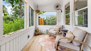 A covered porch with wicker furniture, a fan, and potted plants.