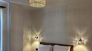 Una cama bien hecha con sábanas y almohadas blancas, cabecera de madera y una lámpara colgante de fibras naturales.